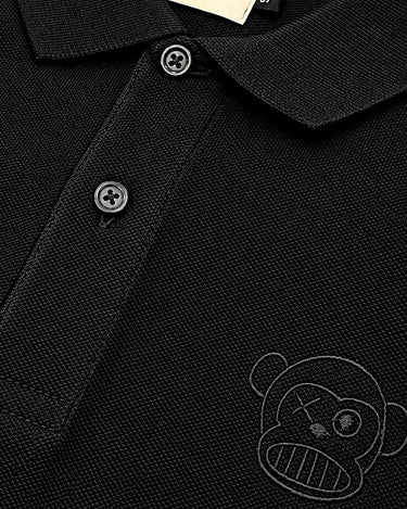 Polo negro con cuello, botones y logo de un mono en el lado izquierdo del pecho.