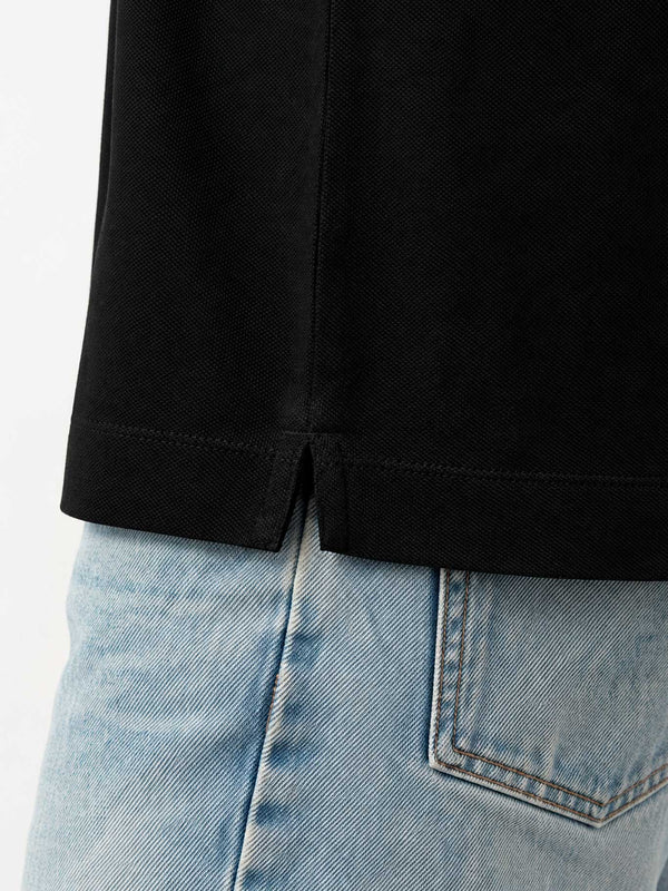 Polo negro para hombre con detalle de abertura en la parte inferior, combinado con jeans claros.