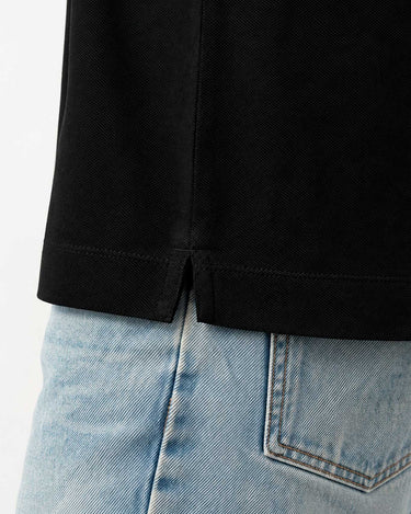 Polo negro para hombre con detalle de abertura en la parte inferior, combinado con jeans claros.