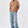 Polo de hombre color caramelo con logo en el pecho, combinado con jeans claros y zapatillas negras.