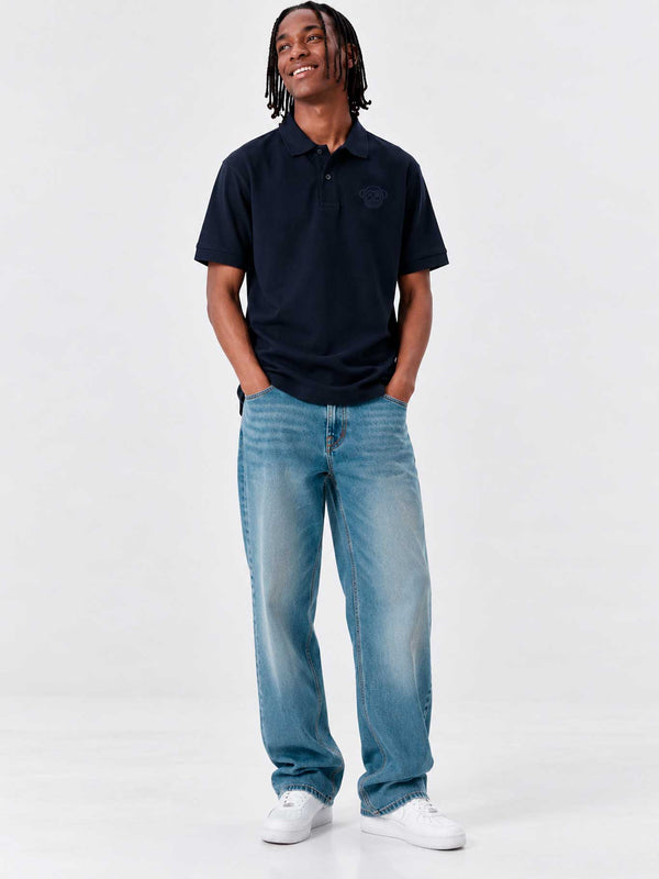 Polo navy de hombre con logo en el pecho, combinado con jeans claros y zapatillas blancas.