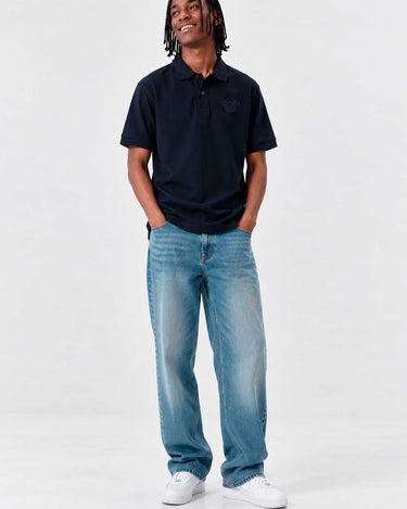Polo navy de hombre con logo en el pecho, combinado con jeans claros y zapatillas blancas.