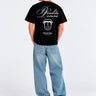 Camiseta negra con texto 'Bendita Locura' y logo de Loco Monky en la espalda, modelo de pie con jeans claros.