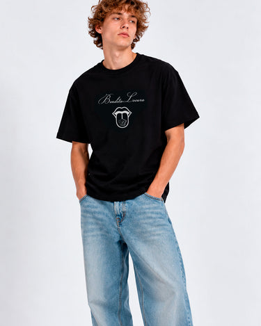 Camiseta negra con diseño gráfico en el pecho, modelo masculino usando jeans claros.