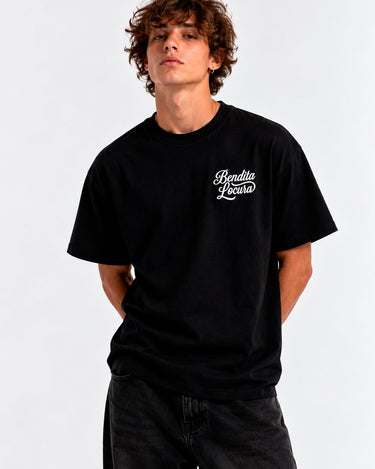 Camiseta negra unisex con texto "Bendita Locura" en el pecho, modelo de hombre con cabello rizado.
