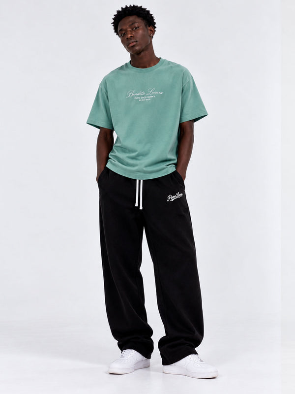 Camiseta verde con bordado en el pecho, combinada con pantalones negros y zapatillas blancas.