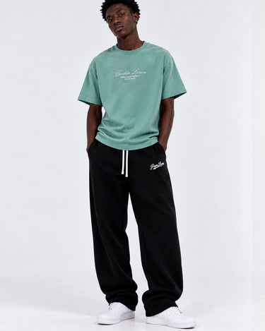 Camiseta verde con bordado en el pecho, combinada con pantalones negros y zapatillas blancas.