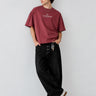 Camiseta boxy color púrpura con texto en el pecho, pantalones negros y zapatillas blancas, modelo de pie.