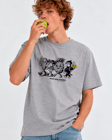 Camiseta gris con estampado de personajes de frutas y texto 'MAKE NEW FRIENDS', modelo sosteniendo una manzana.