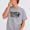 Camiseta gris con estampado de personajes de frutas y texto 'MAKE NEW FRIENDS', modelo sosteniendo una manzana.