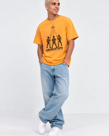 Camiseta amarilla con diseño de tres figuras y texto 'GODBUSTERS', pantalones jeans claros y zapatillas blancas.