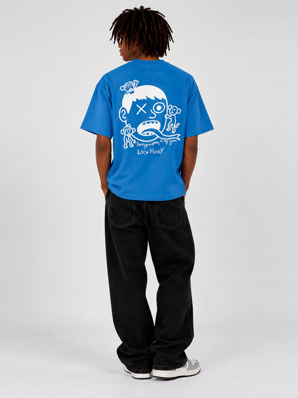 Camiseta azul con diseño gráfico en la espalda, hombre de pie con pantalones negros.