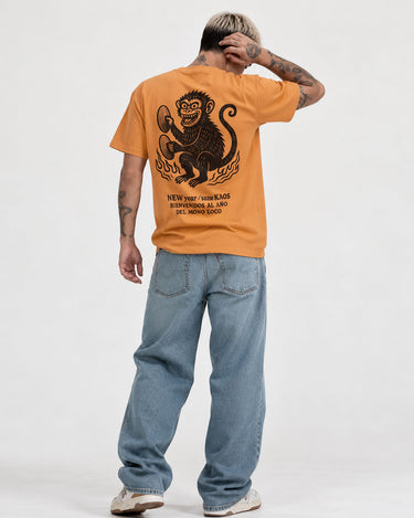 Camiseta mostaza con diseño de mono en la espalda, texto en negro, pantalones de mezclilla claros.