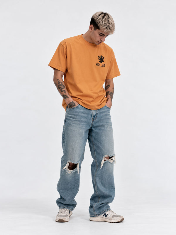 Camiseta mostaza con diseño en el pecho, combinada con jeans rotos y zapatillas blancas.