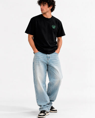 Camiseta negra con bordado verde en el pecho, combinada con jeans claros y zapatillas negras.