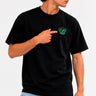 Camiseta negra con bordado verde de un mono en el pecho, modelo señalando el diseño.