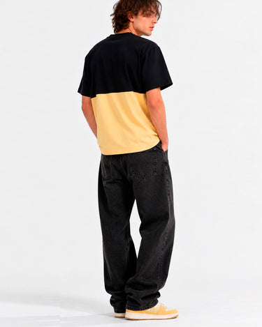 Camiseta de hombre en amarillo y negro, con diseño de bloques de color, vista trasera, combinada con pantalones oscuros.