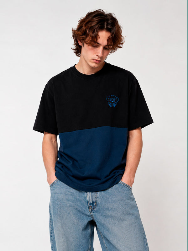 Camiseta de hombre en azul oscuro y negro con logo de mono en el pecho, modelo con jeans claros.