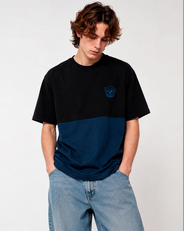 Camiseta de hombre en azul oscuro y negro con logo de mono en el pecho, modelo con jeans claros.