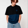 Camiseta de hombre en azul oscuro y negro con logo de mono en el pecho, modelo con jeans claros.