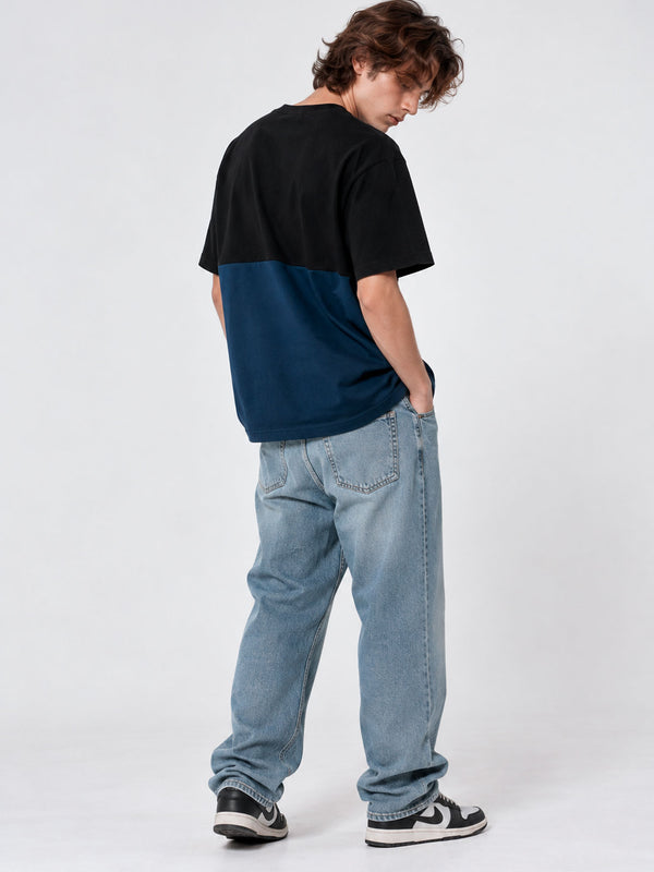 Camiseta de hombre en azul oscuro y negro, con diseño de bloques de color, vista trasera, combinada con jeans claros.