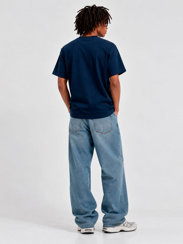 Camiseta de color azul oscuro vista trasera, combinada con jeans claros y zapatillas deportivas.