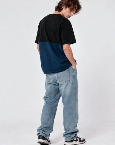 Camiseta de hombre en azul oscuro y negro, con diseño de bloques de color, vista trasera, combinada con jeans claros.