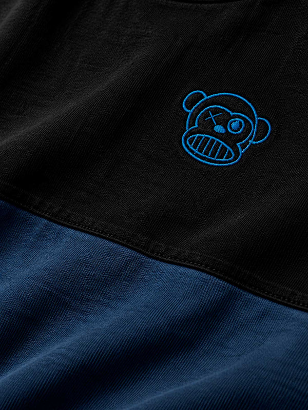 Camiseta en azul oscuro y negro con bordado de un mono sonriente en el pecho.