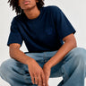 Camiseta azul oscuro con diseño de oso en el pecho, modelo sentado con pantalones claros y zapatillas deportivas.