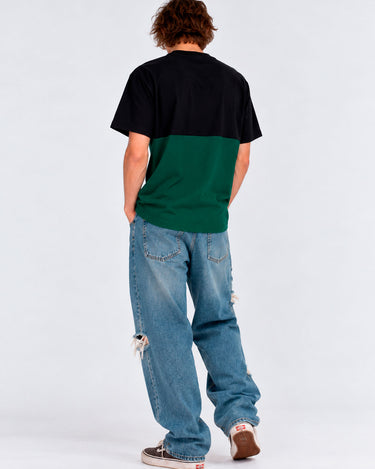 Camiseta de hombre en verde oscuro y negro, vista trasera, combinada con jeans claros y zapatillas.