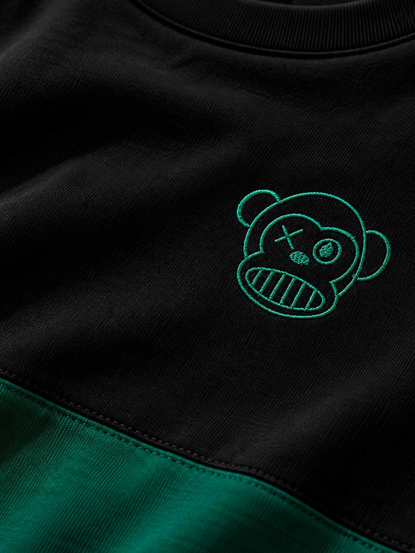 Camiseta negra con detalles en verde oscuro y bordado de un oso con cara sonriente y ojos cruzados