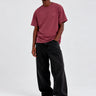 Camiseta de color púrpura con bordado en el pecho, modelo masculino con pantalones oscuros y zapatillas blancas.