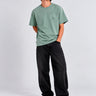 Camiseta verde con bordado en el pecho, combinada con pantalones negros y zapatillas deportivas blancas.