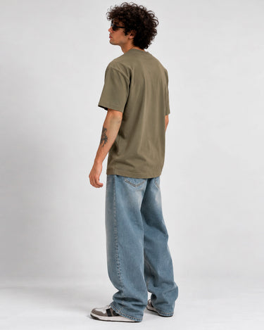 Camiseta de hombre color oliva, vista trasera, con pantalones anchos de mezclilla y zapatillas deportivas.