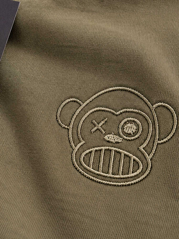 Camiseta color oliva con bordado de un mono con un ojo cerrado y una hoja en el lado derecho.