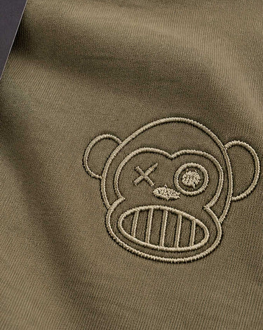 Camiseta color oliva con bordado de un mono con un ojo cerrado y una hoja en el lado derecho.