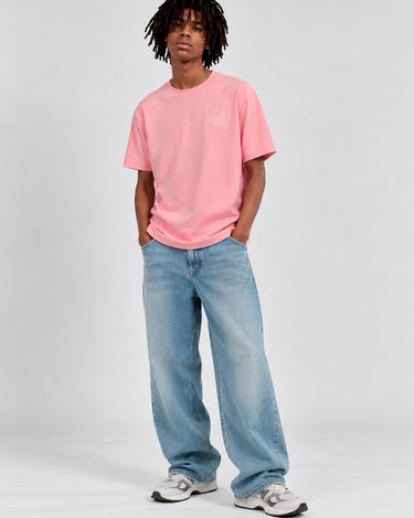 Camiseta rosa con logo en el pecho, combinada con jeans claros y zapatillas deportivas.