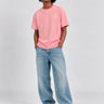 Camiseta rosa con logo en el pecho, combinada con jeans claros y zapatillas deportivas.