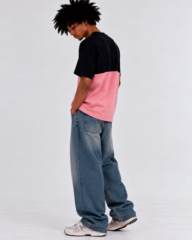 Camiseta de hombre en rosa y negro, con diseño de bloques de color, combinada con jeans anchos.