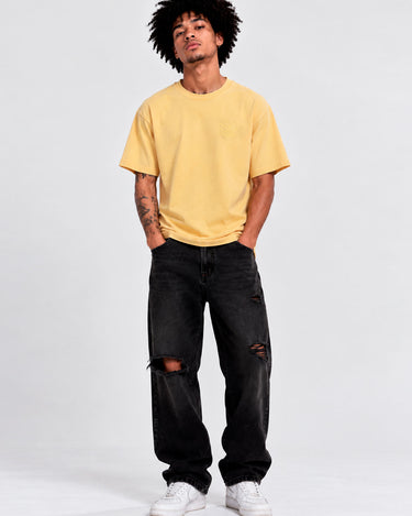 Camiseta amarilla de hombre con logo en el pecho, combinada con jeans negros y zapatillas blancas.