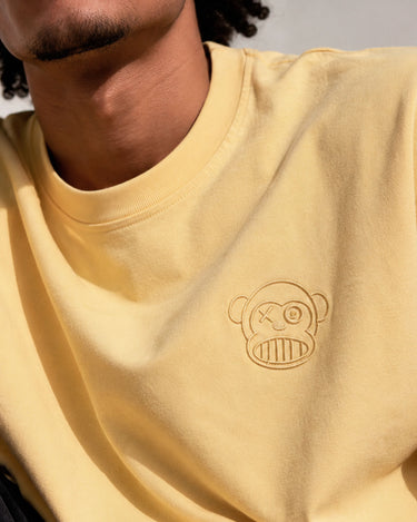 Camiseta amarilla con bordado de un mono con un ojo y sonrisa, detalle en el pecho.
