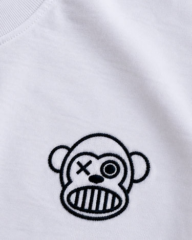 Camiseta blanca con bordado de un mono con un ojo cruzado y una boca de rayas en el pecho.
