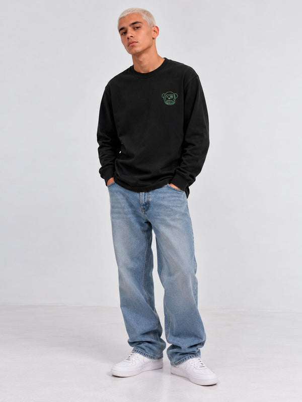 Camiseta de manga larga negra con diseño de mono en el pecho, combinada con jeans claros y zapatillas blancas.