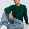 Camiseta de manga larga color verde oscuro, con logo en el pecho, combinada con jeans claros y zapatillas blancas.