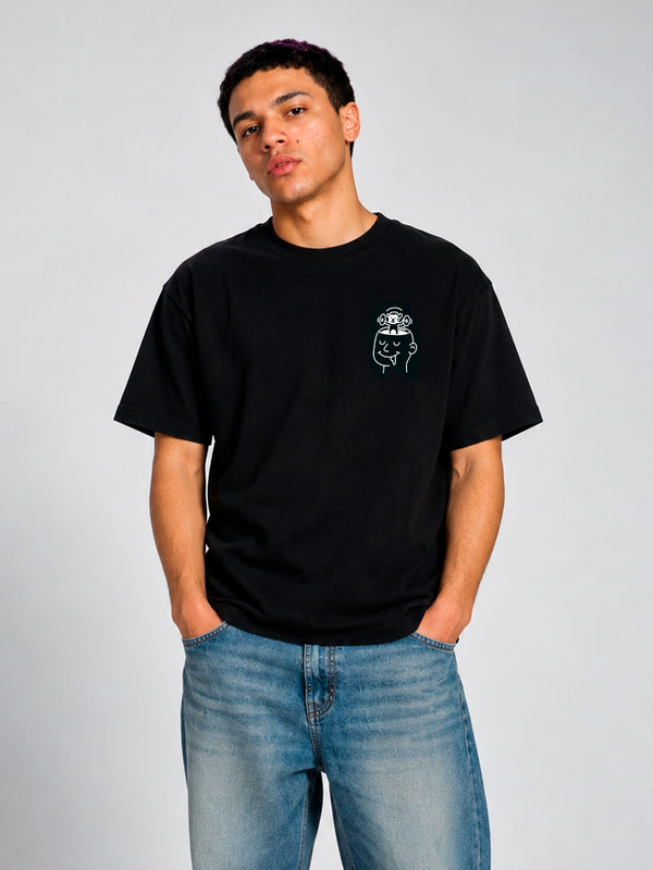 Camiseta negra con diseño en el pecho, modelo masculino con manos en los bolsillos, fondo claro.