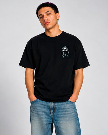 Camiseta negra con diseño en el pecho, modelo masculino con manos en los bolsillos, fondo claro.