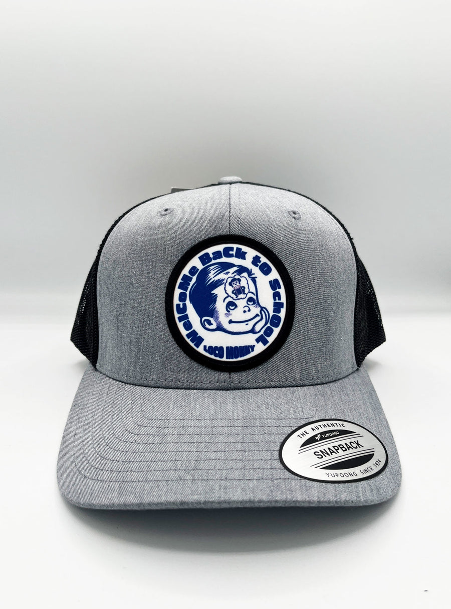 Gorra trucker Welcome Back de Loco Monky, gris con rejilla y parche "Welcome Back to School" en el frente.