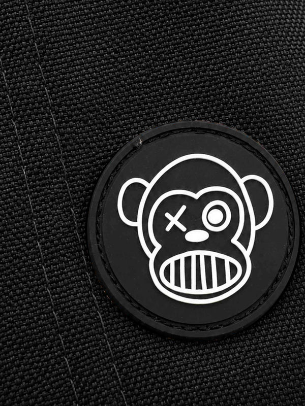 Parche negro con diseño de mono sonriente y ojos diferentes sobre fondo de tela negra.
