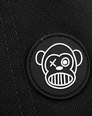 Parche negro con diseño de mono sonriente y ojos diferentes sobre fondo de tela negra.