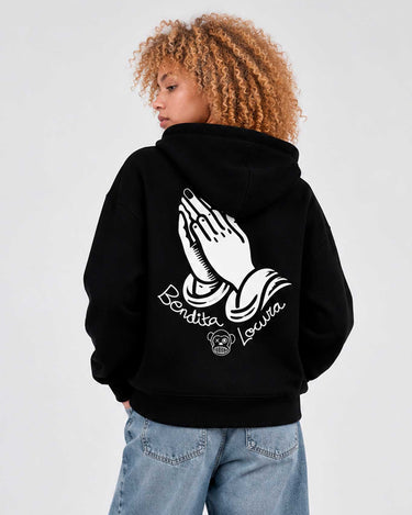 Sudadera negra con capucha, diseño de manos en oración y texto 'Bendita Locura' en la parte posterior.